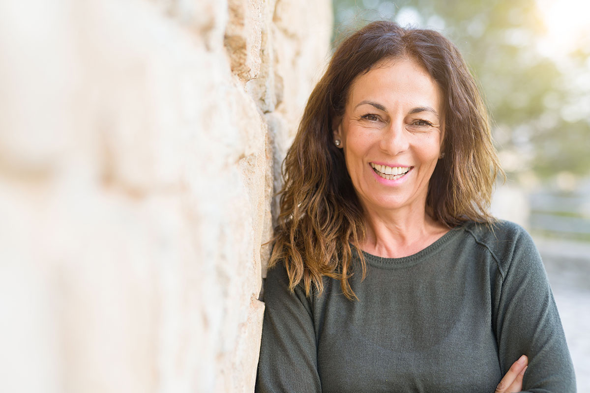 benefits of residential treatment middle aged woman smiling next to rock wall because of benefits of residential treatment