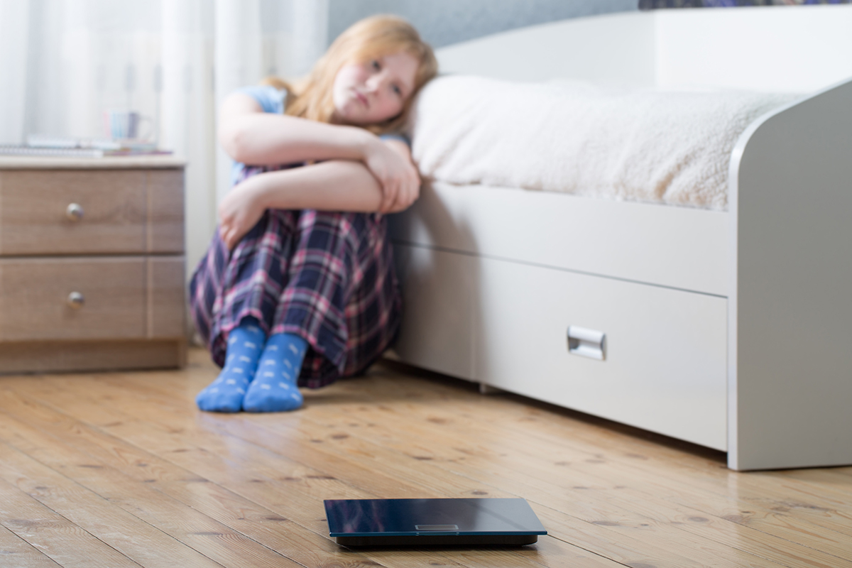 a young girl sits on the floor of her bedroom as she considers body image and social media